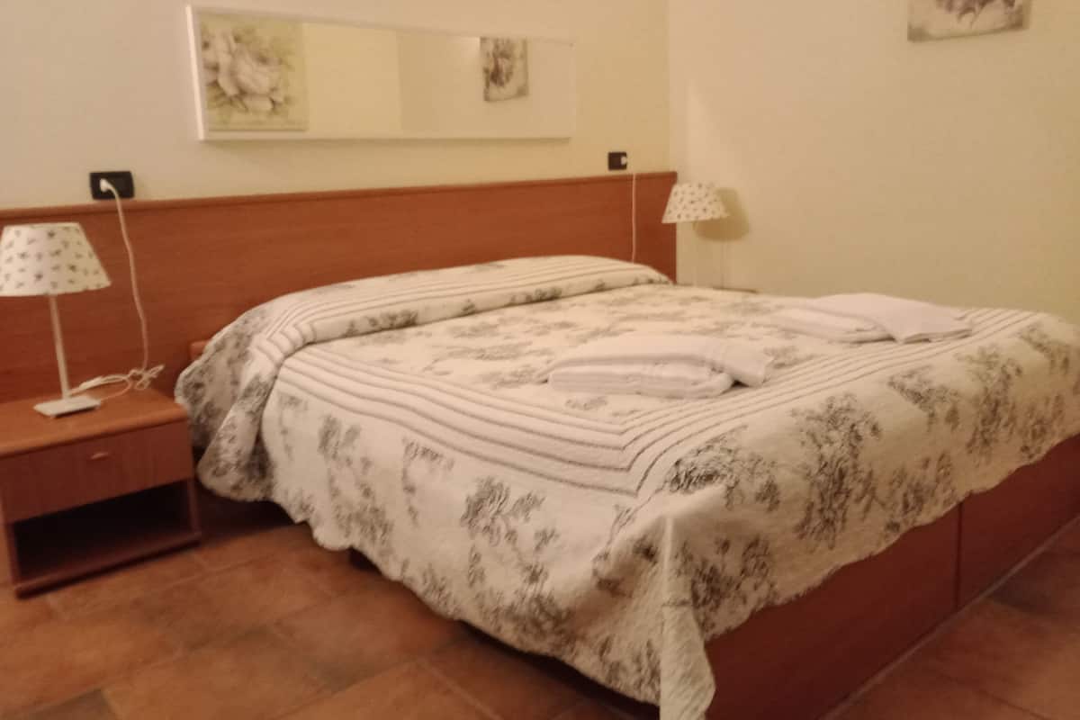 Una cama bien hecha con una colcha estampada con motivos florales, una lámpara de noche y una mesita de noche con un teléfono.