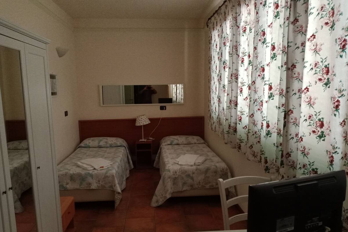 Una habitación con dos camas, un escritorio, una computadora, un espejo y cortinas con estampado floral.