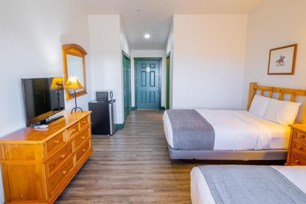 A hotel room with a bed, a TV, a dresser, and a desk. - Teton Valley Motel (Victor)