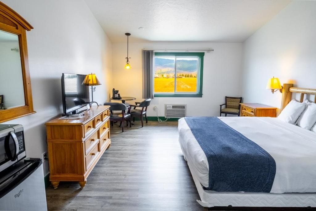 Ein Hotelzimmer mit Bett, Schreibtisch, Stuhl, Fernseher und Blick auf ein Feld durch ein Fenster.