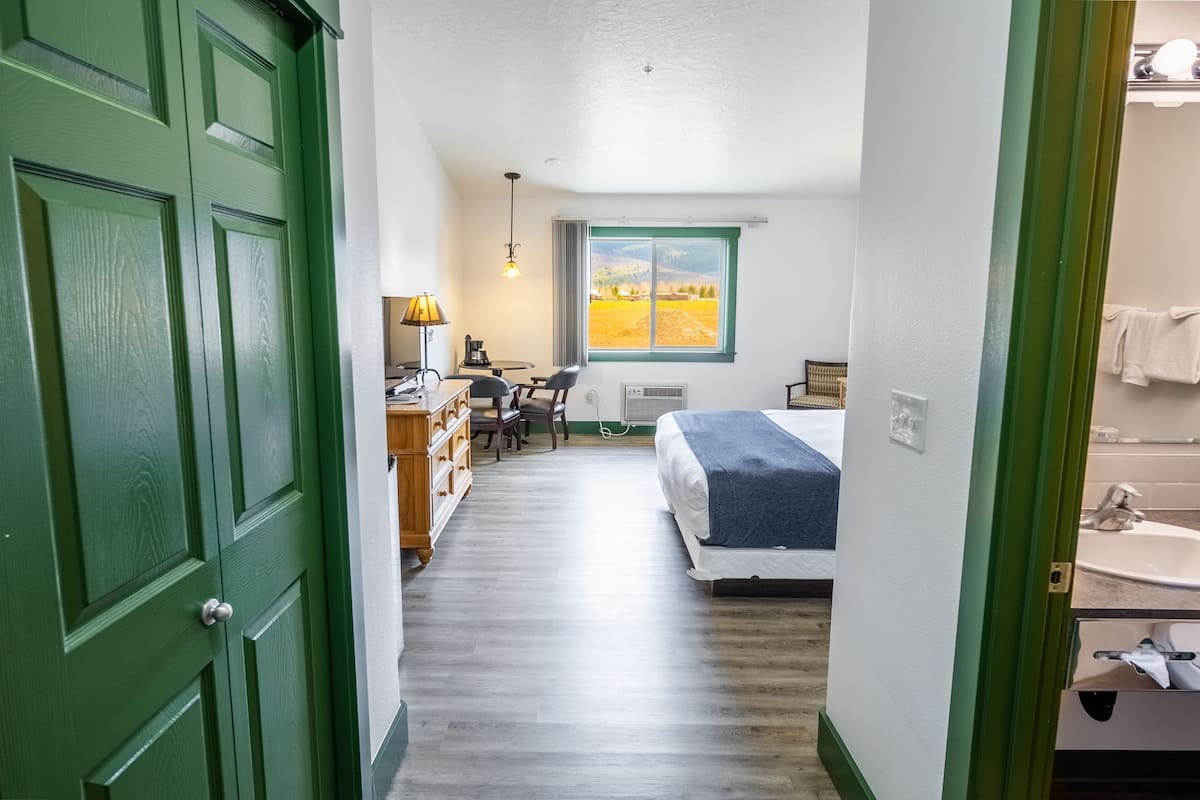 A narrow hallway leading to a bedroom with a bed, a desk, and a chair. A window with a view of a field is visible.