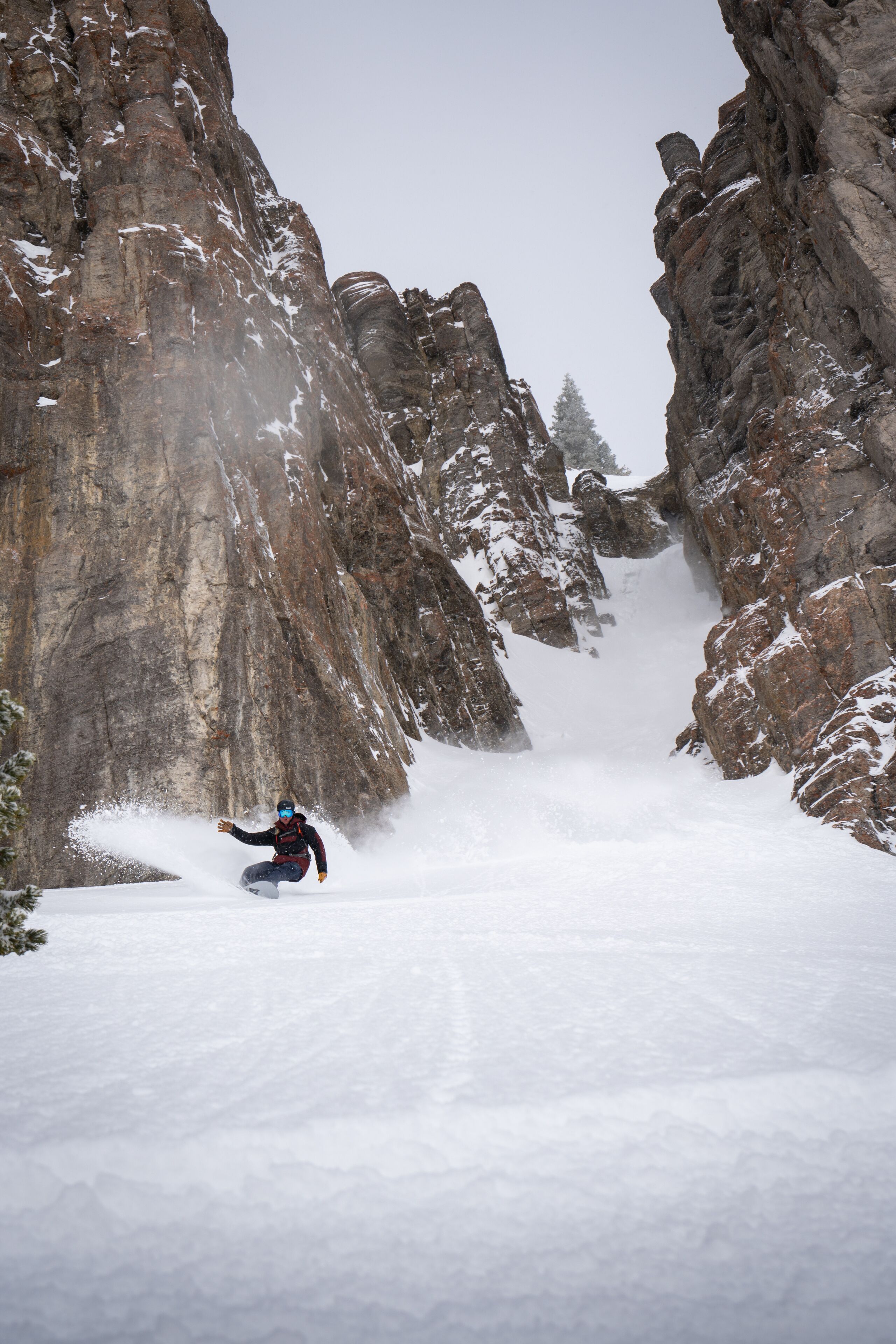 A person skiing down a snow-covered mountain path between rocky cliffs.