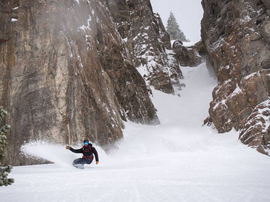A person skiing down a snow-covered mountain path between rocky cliffs.
