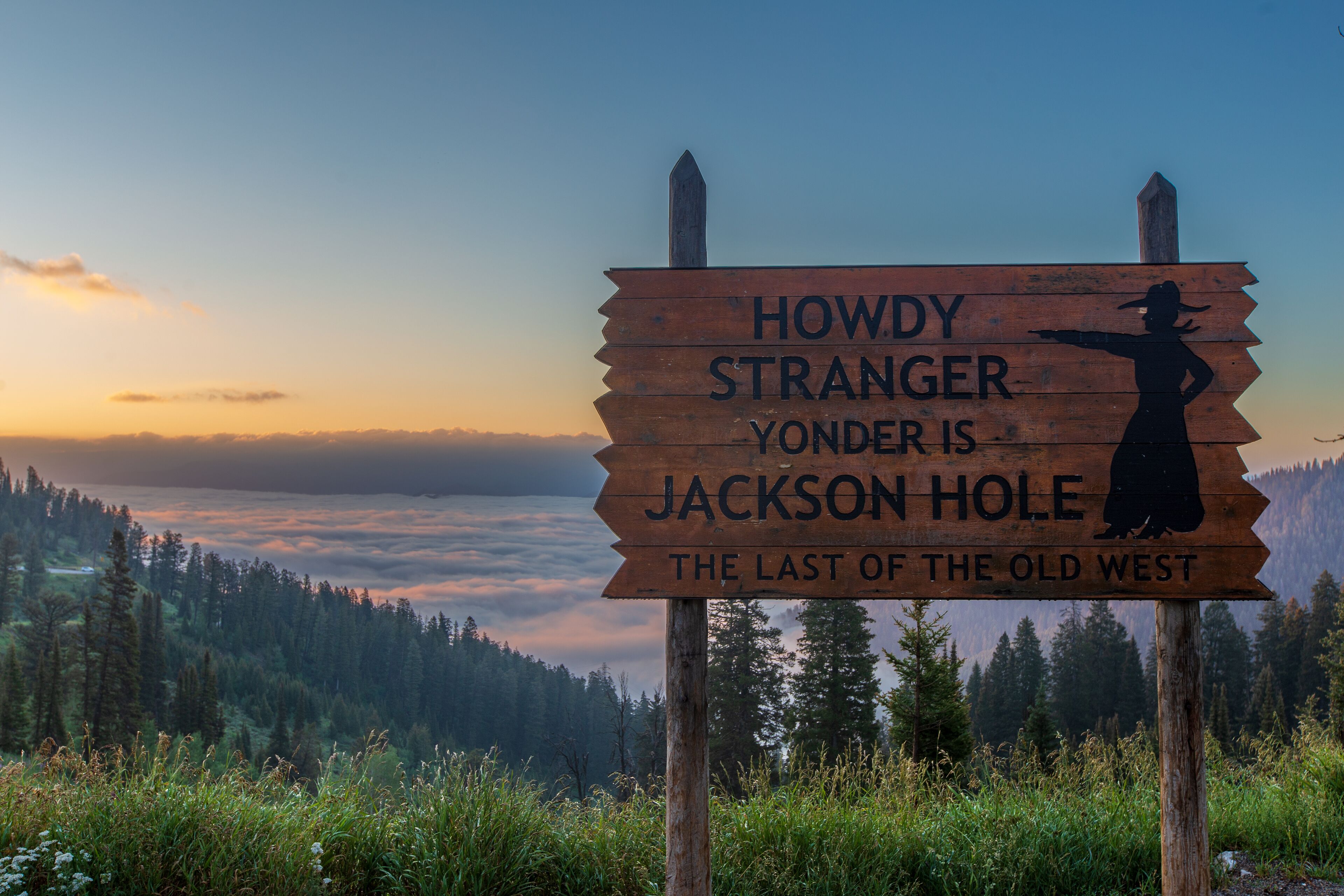 Un cartello di legno con la sagoma di una donna che indica la scritta 'Howdy Stranger Yonder is Jackson Hole The Last of the Old West'.