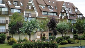A multi-story residential building with a sloped roof, balconies, and a small garden area with flowers and shrubs. - Résidence Lagrange Vacances Villers-sur-Mer (Villers-sur-Mer)