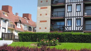 A multi-story residential building with a mix of brick and timber framing, balconies, and a well-maintained garden with flowering plants. - Résidence Lagrange Vacances Villers-sur-Mer (Villers-sur-Mer)