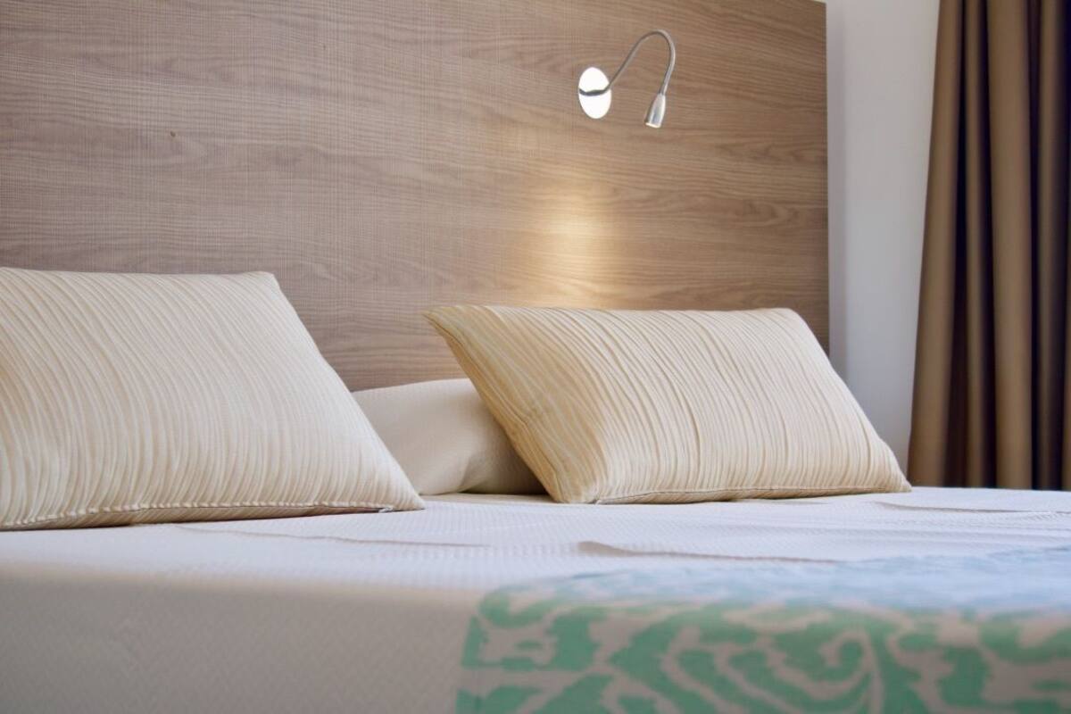 A neatly made bed with two pillows, a headboard with a light fixture, and a patterned bedspread.