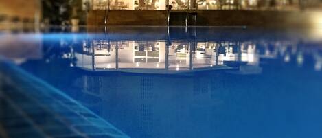 A swimming pool reflecting a building with a glass facade and interior lighting.