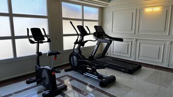 Un gimnasio con dos bicicletas estáticas y una cinta de correr, ventanas amplias y piso de baldosas.