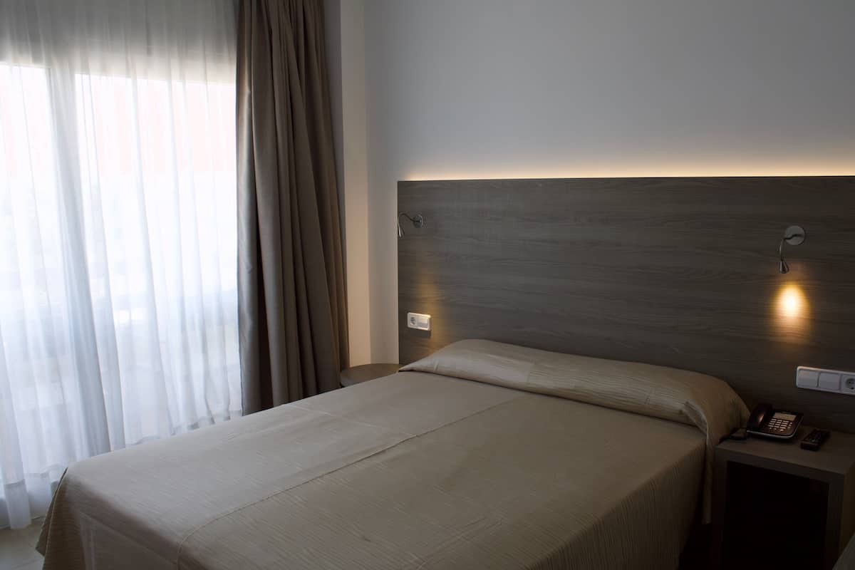 A hotel room with a bed, bedside table, and a wall-mounted phone.