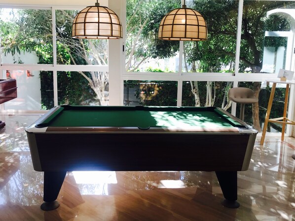A pool table in a room with large windows and hanging lamps.