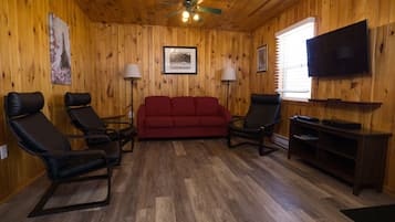 A wooden-paneled room with a red sofa, two black chairs, a television, and two floor lamps.