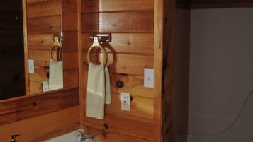 Un baño con paneles de madera, un lavamanos, un espejo, un tocaderechos y un inodoro.