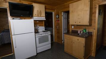 Une cuisine de taille réduite, équipée d’un réfrigérateur, d’une cuisinière et de meubles de rangement en bois.