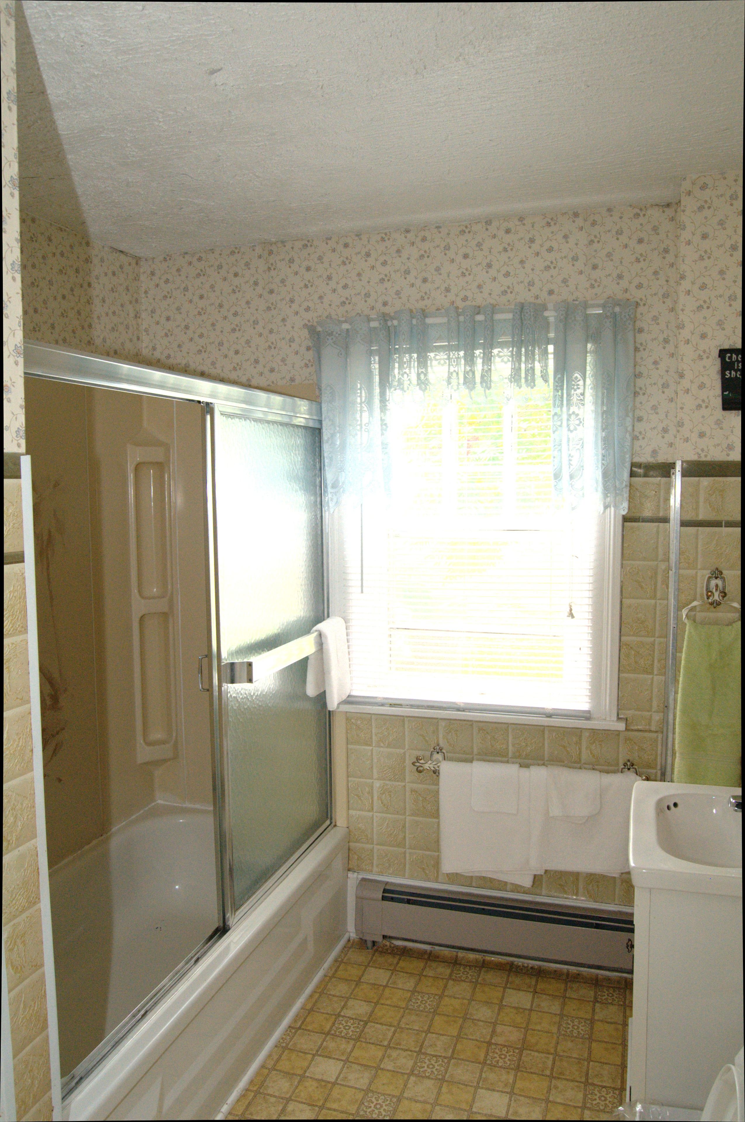 A bathroom with a shower, a window with curtains, a bathtub, and a sink.