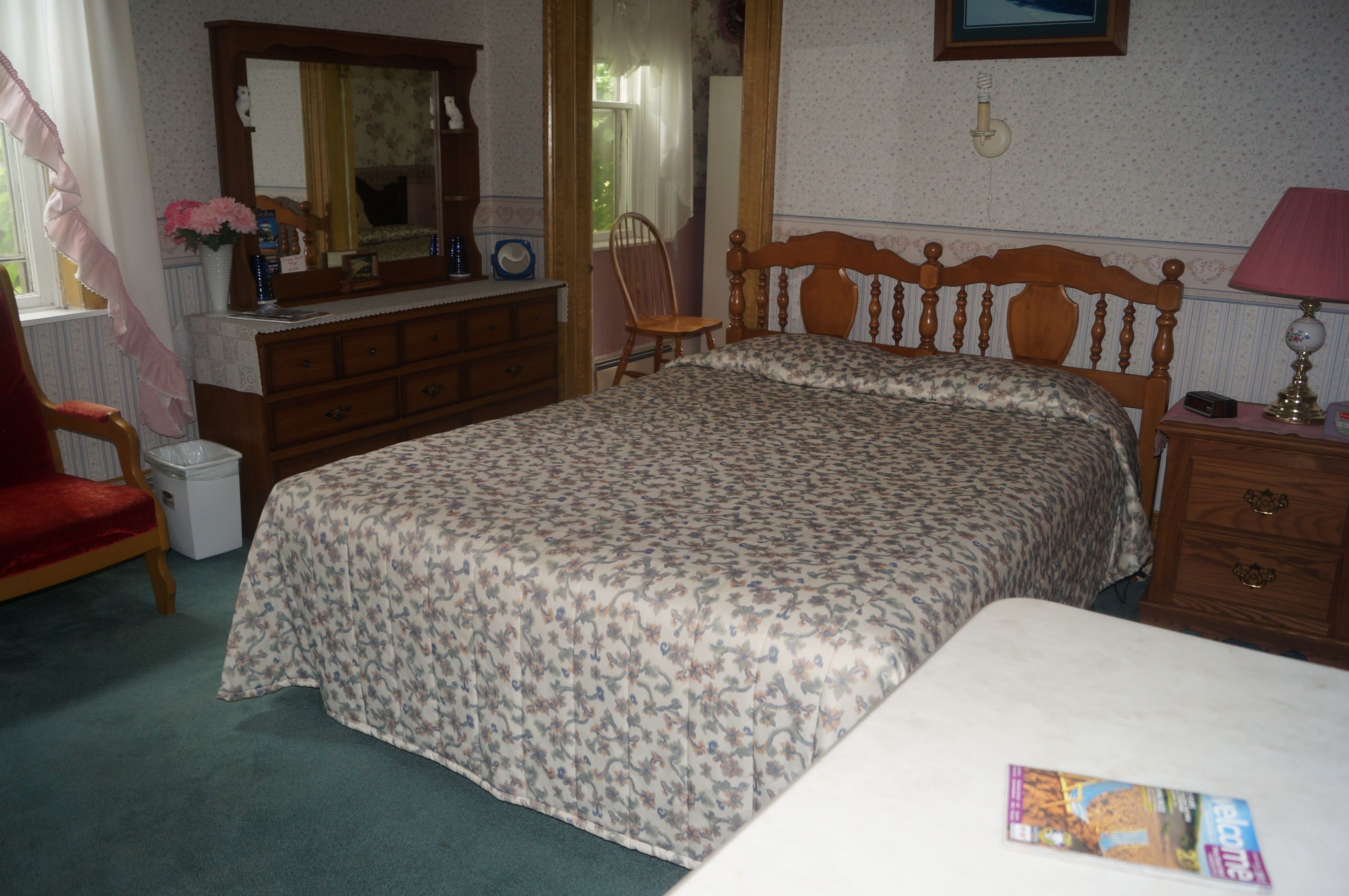 Une chambre à coucher comprenant un lit, une commode, une chaise et une table de chevet avec une lampe.