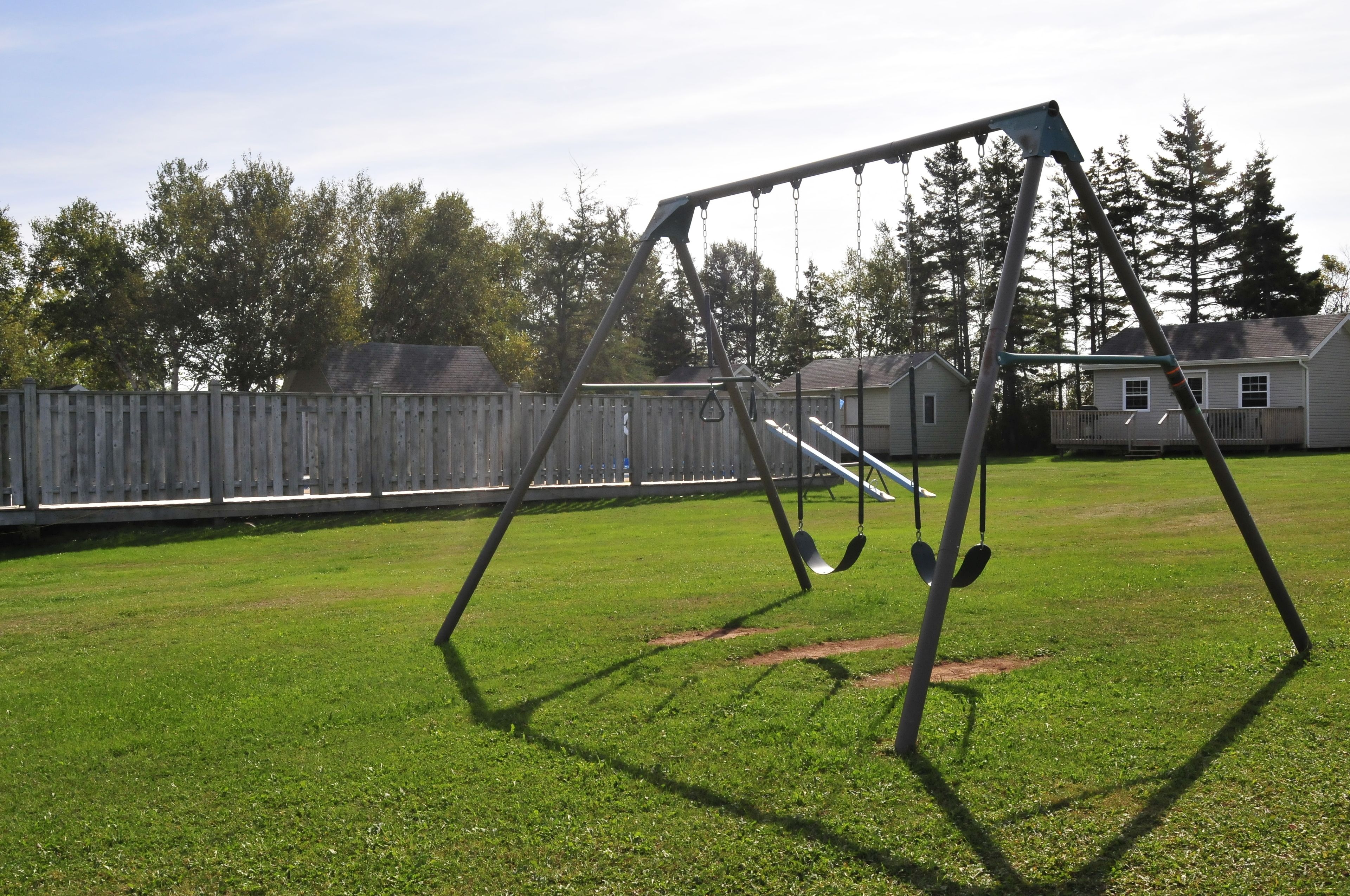 A swing set in a grassy yard with a wooden fence and houses in the background.