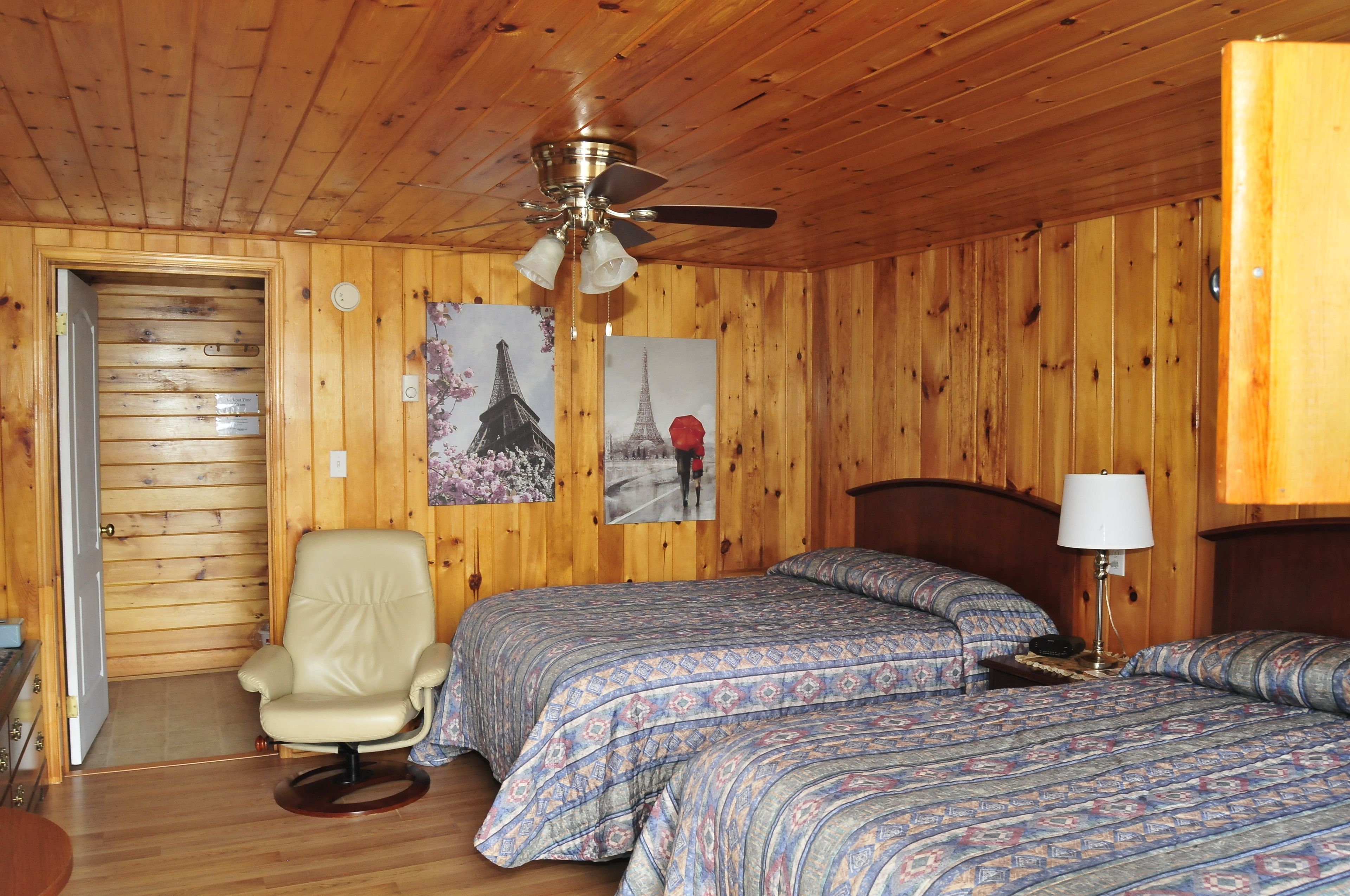 A wooden-paneled room with two beds, a ceiling fan, and a door.
