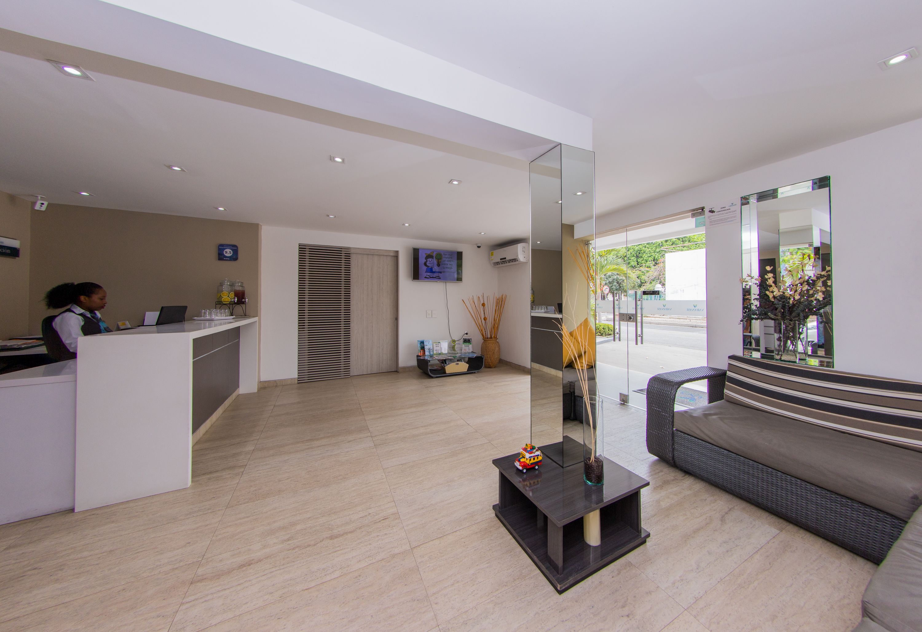 A modern reception area with a reception desk, a sofa, a TV, and a large mirror.
