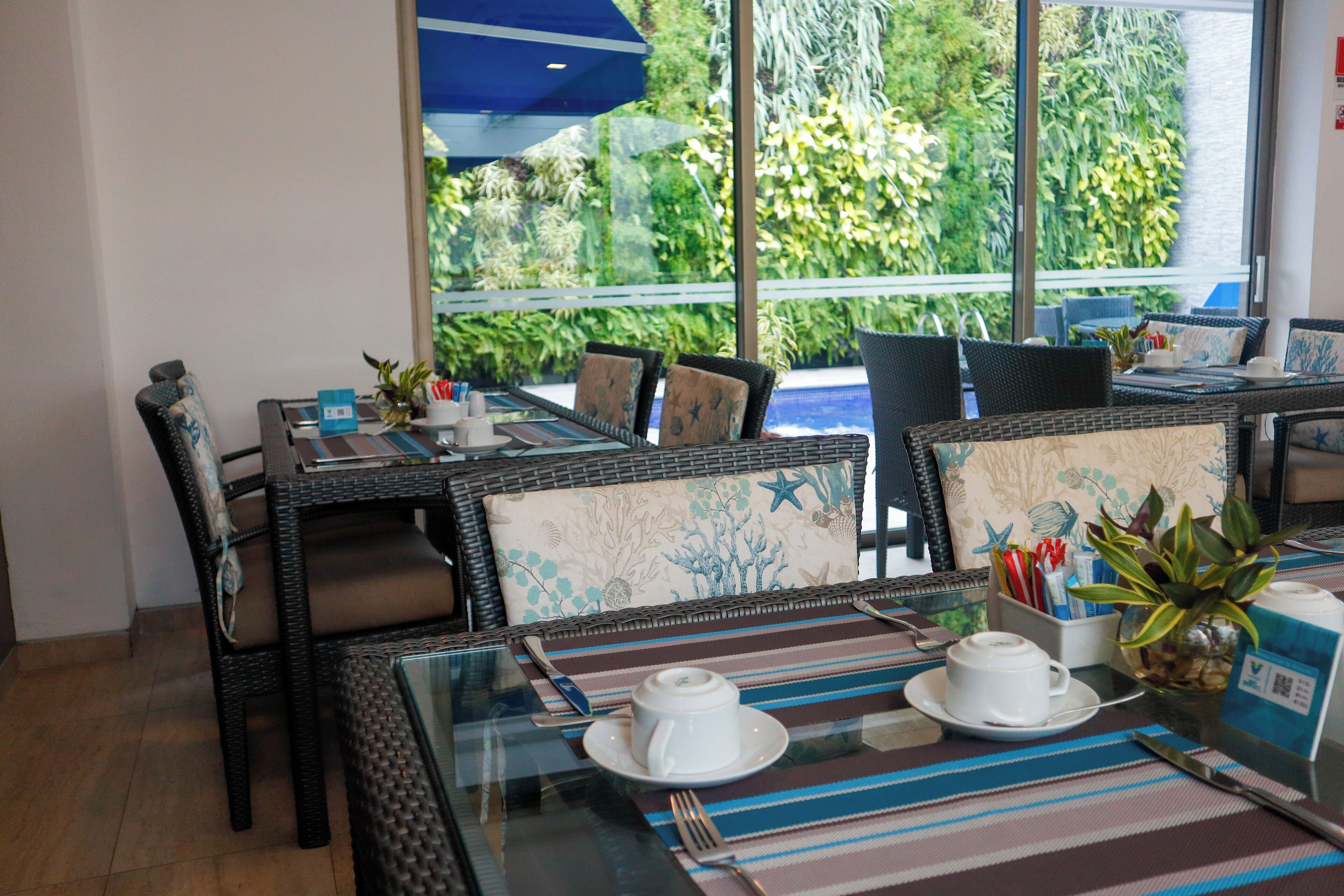 A dining area with wicker furniture, a glass table, and a view of a pool and greenery.
