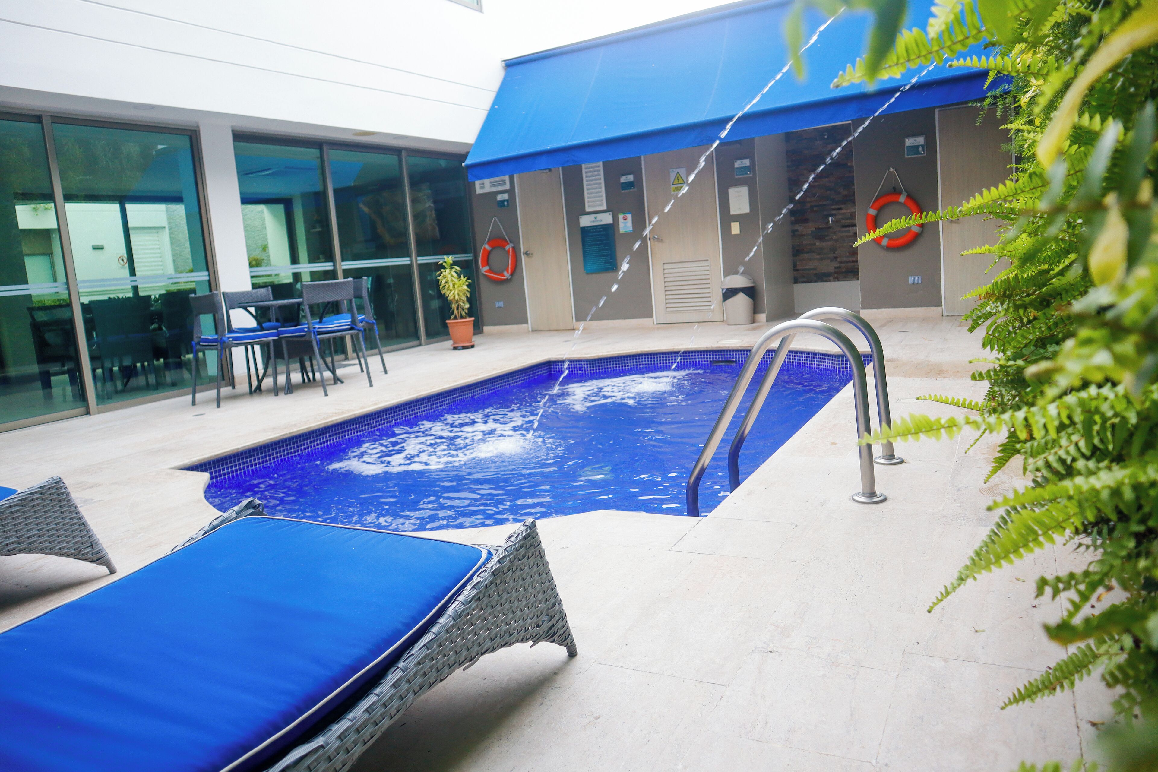 Una piscina con sillones de descanso, una planta en maceta y un toldo azul.