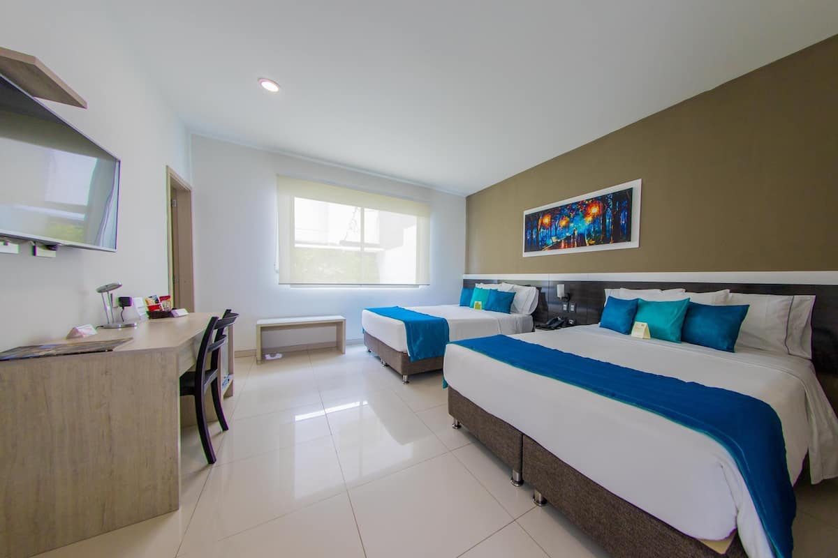 A hotel room with two beds, a desk, a chair, a window, and a painting on the wall.