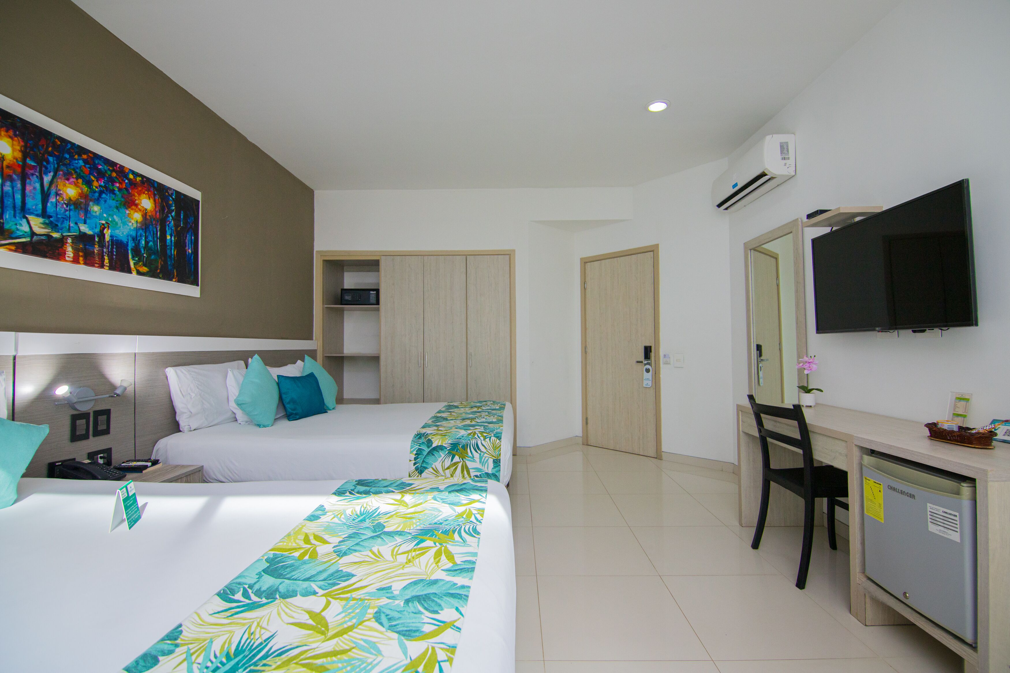 A hotel room with two beds, a desk, a TV, and a painting on the wall.