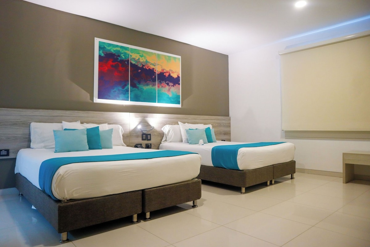 A hotel room with two beds, a large abstract painting on the wall, and a window with blinds.