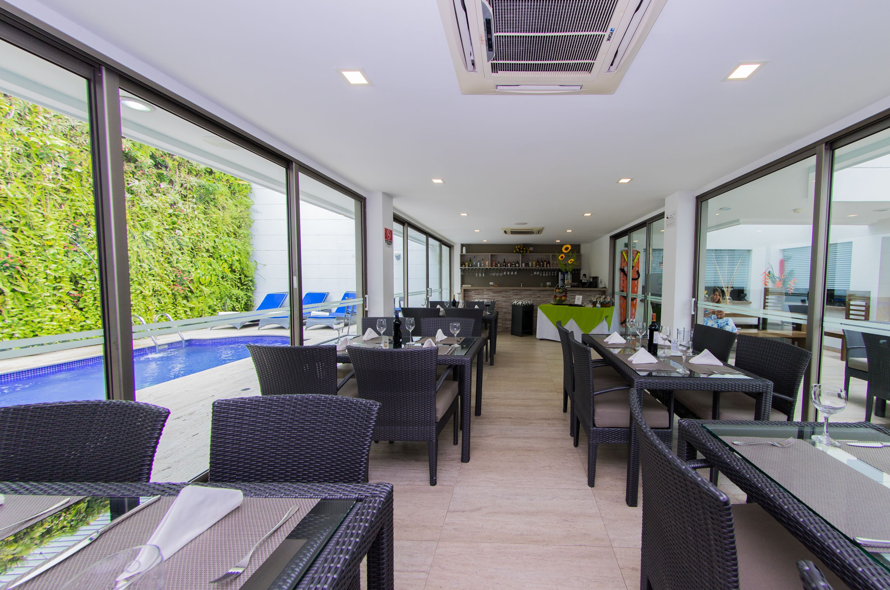 Un ristorante con posti a sedere all'aperto affacciato su una piscina, con arredi in vimini e interni moderni.