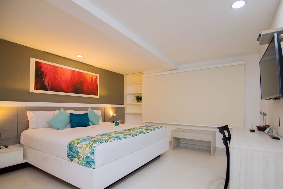 A modern hotel room with a large bed, a flat-screen TV, a desk, and a wall-mounted TV.