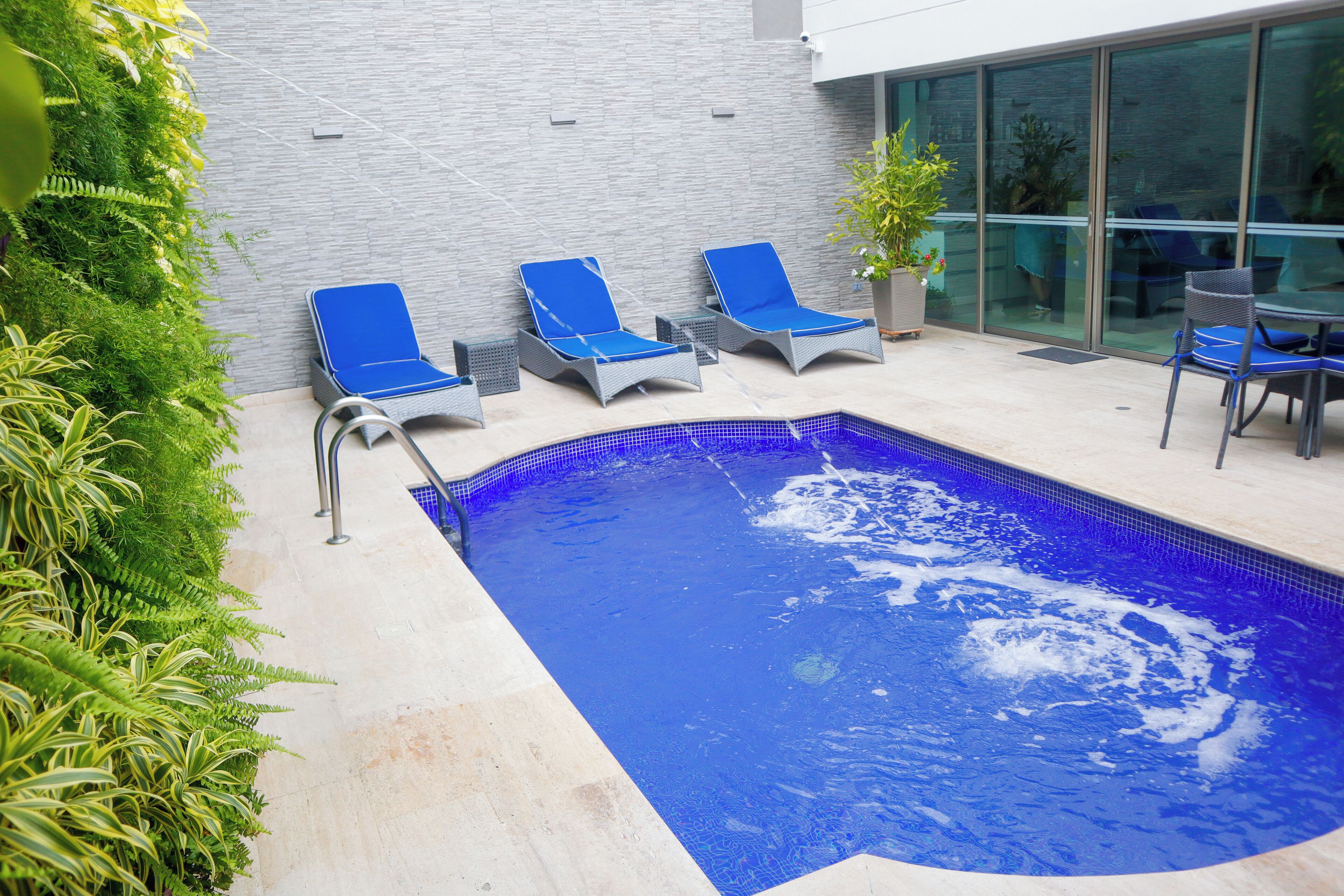 A swimming pool with blue tiles, surrounded by lounge chairs and potted plants.