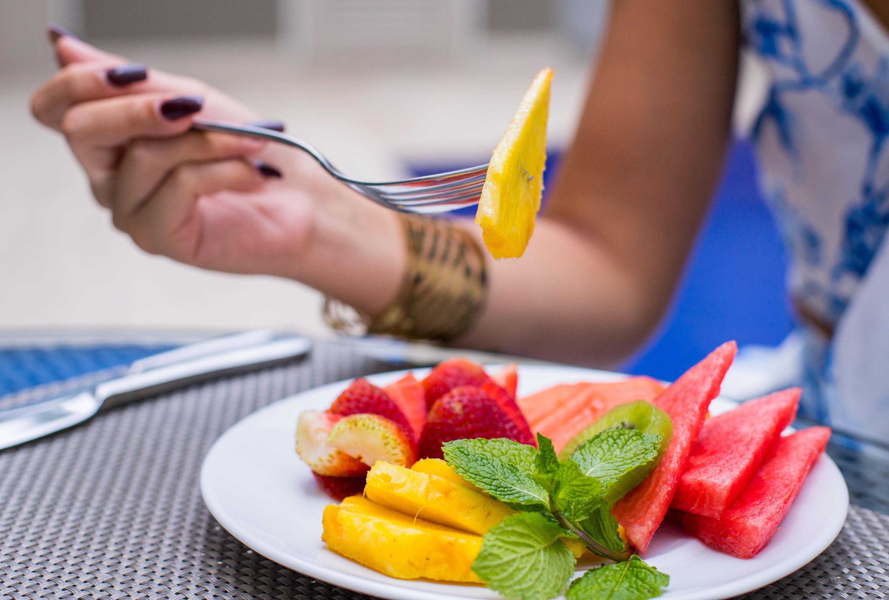A plate of sliced fruits including watermelon, strawberries, and mango, with a fork holding a slice of mango.