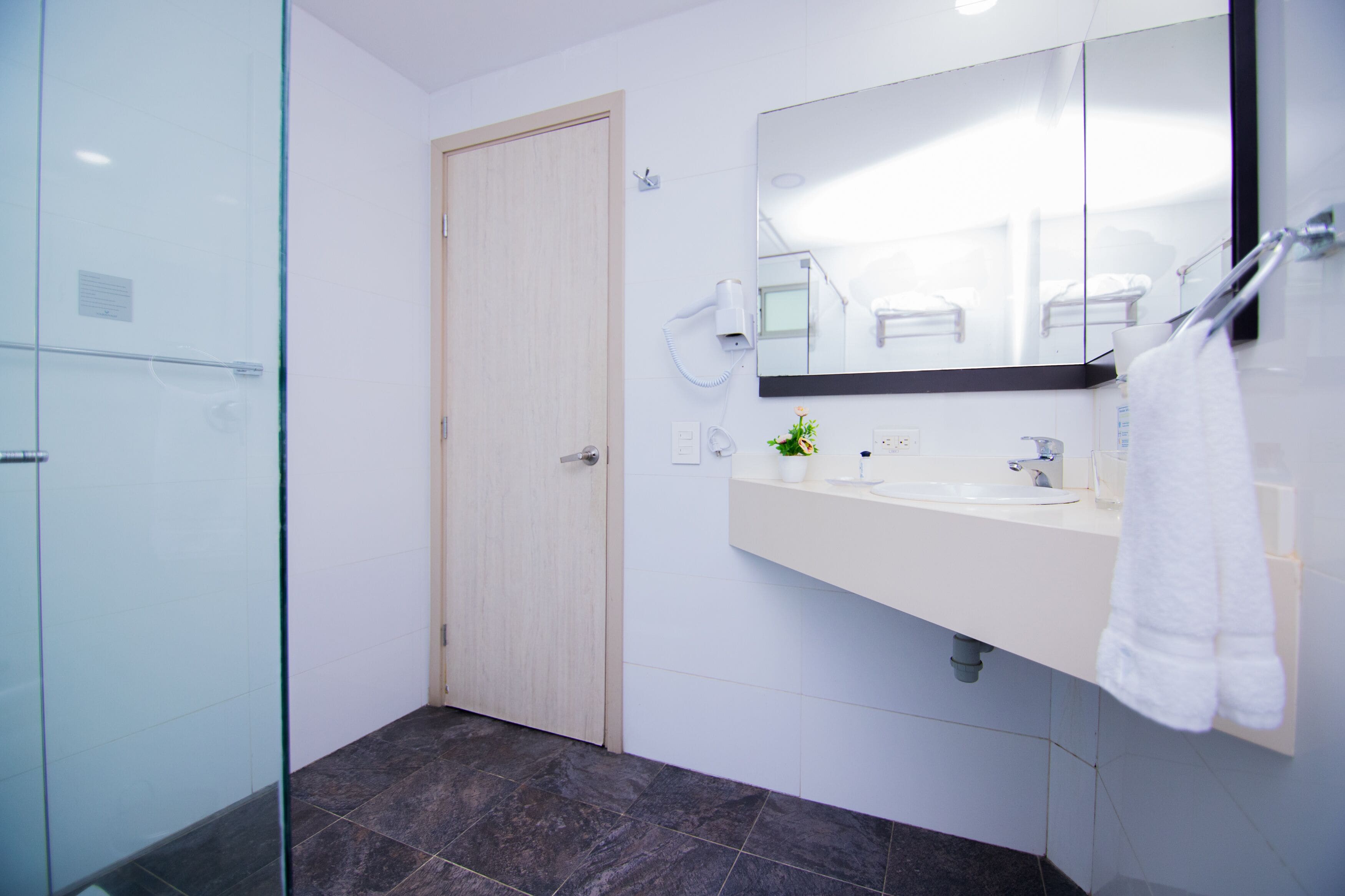 Un baño moderno con cabina de ducha de vidrio, un lavabo blanco con espejo y una toalla colgada en la pared.