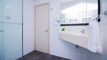 Un baño moderno con cabina de ducha de vidrio, un lavabo blanco con espejo y una toalla colgada en la pared.