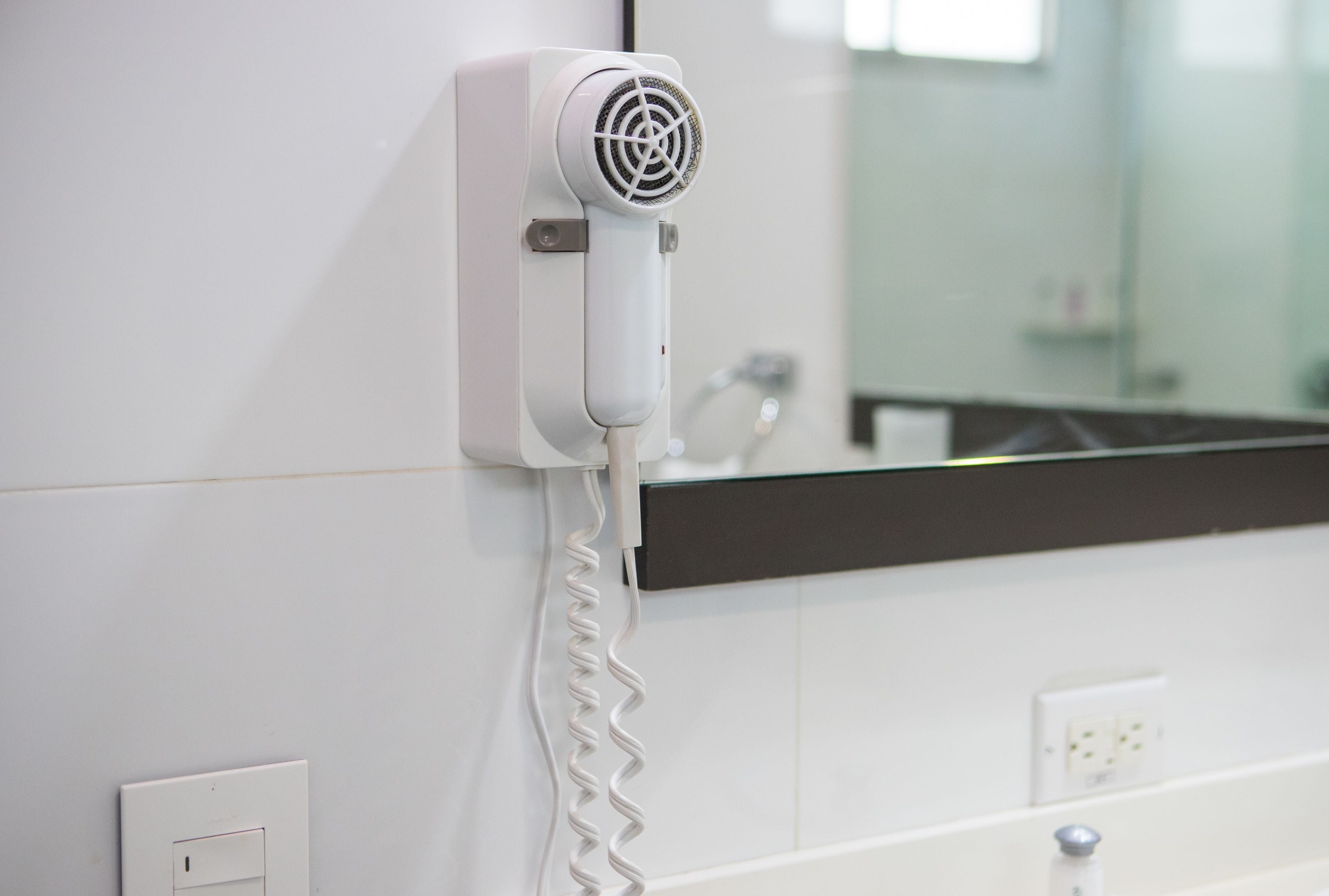 A hair dryer mounted on a white wall with a mirror above it.