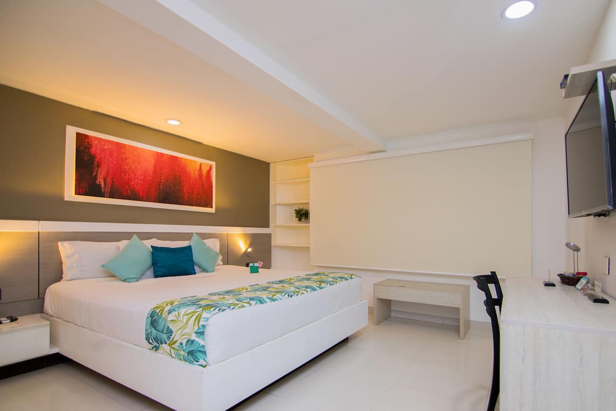 A modern hotel room with a large bed, a flat-screen TV, a bedside table, and a bench.