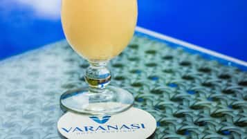 Cóctel con pajita y cereza, decorado con una rodaja de piña y una hoja, sobre un posavasos con el logotipo del Hotel Varanaasi.