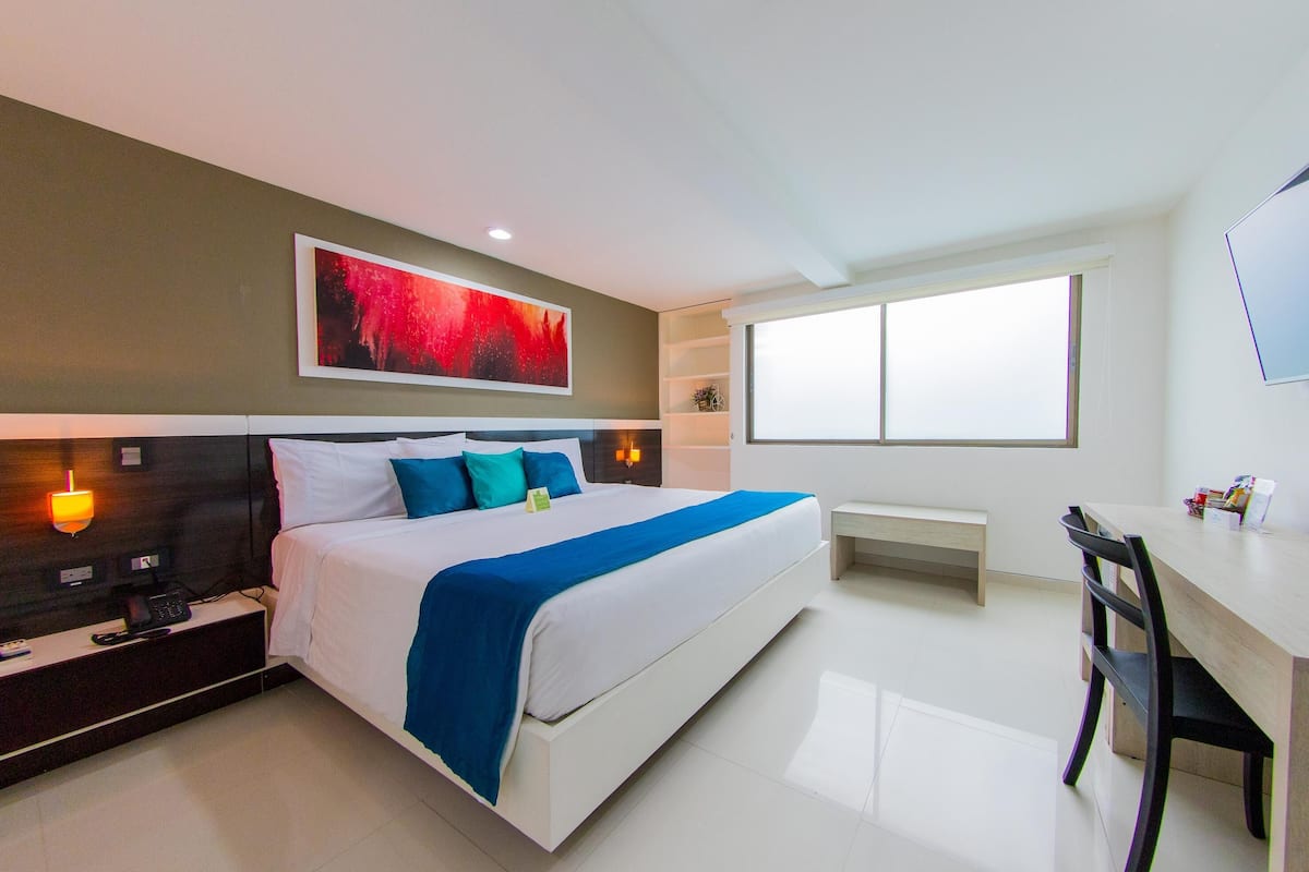 A modern hotel room with a large bed, bedside tables, a desk, and a window.