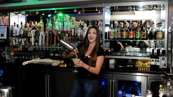 A bar area with a bartender preparing a drink, shelves stocked with various bottles, and a refrigerator.