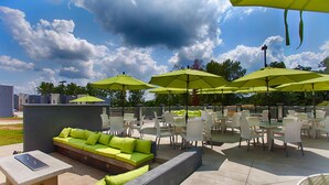Un espace extérieur aménagé en terrasse, avec des sièges et des tables sous des parasols verts, un foyer et une vue sur le ciel.
