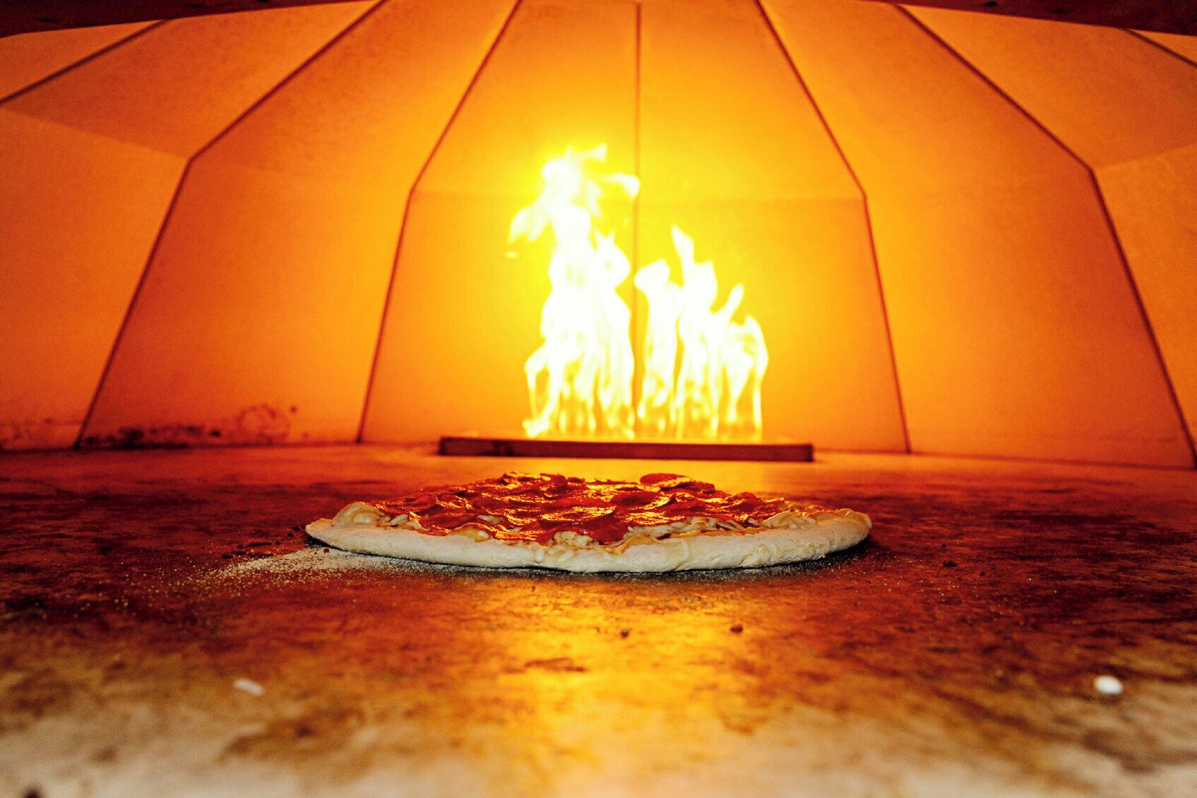 Una pizza en un horno de leña, con un fuego brillante al fondo.