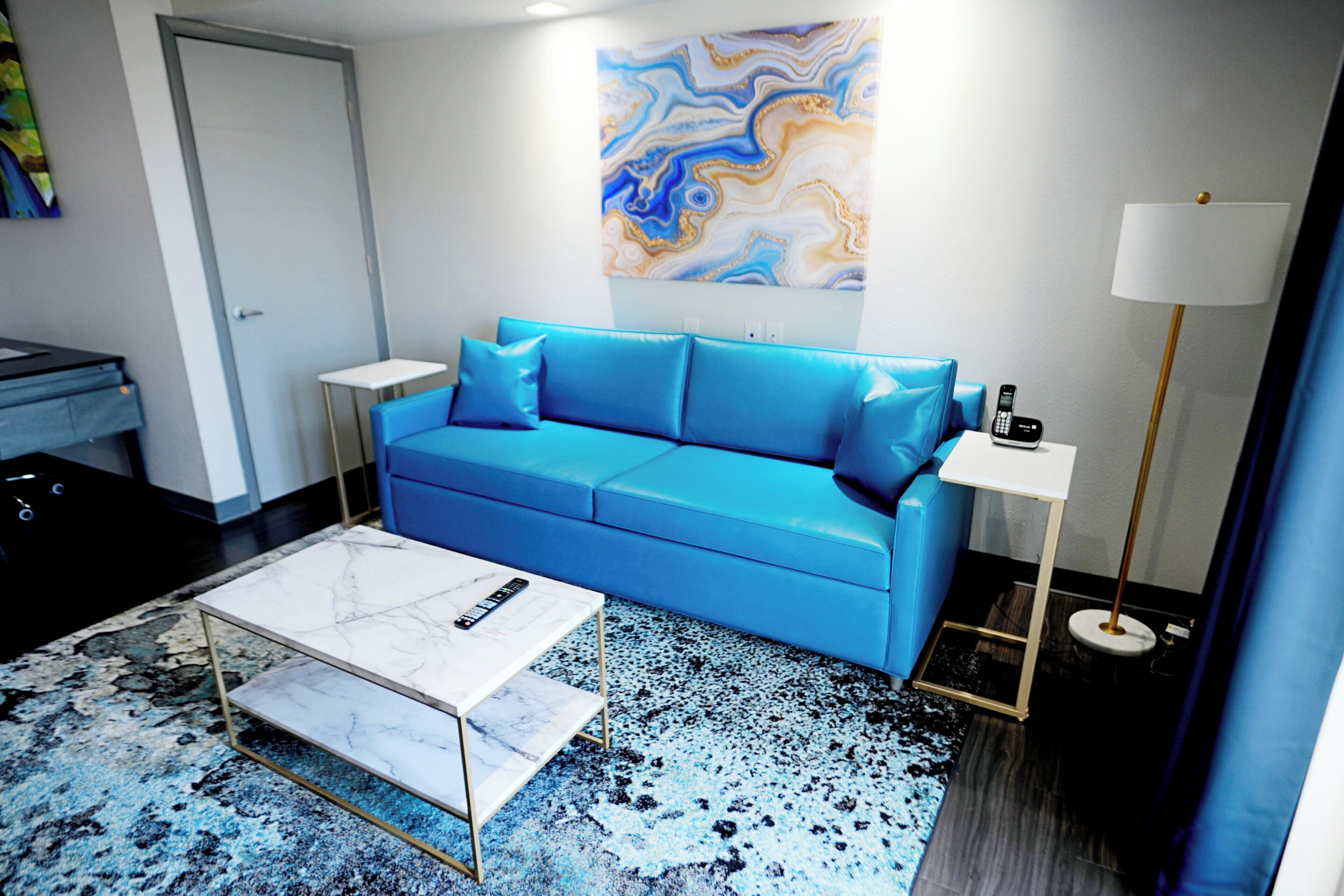 Ein modernes Wohnzimmer mit einem blauen Sofa, einem weißen Couchtisch, einem Boden mit Marmoroptik und einem Wandkunstwerk.