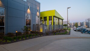 Un bâtiment moderne à la façade grise, agrémenté d’une section jaune vif, doté de grandes fenêtres et d’un espace paysager planté d’arbustes et de fleurs.