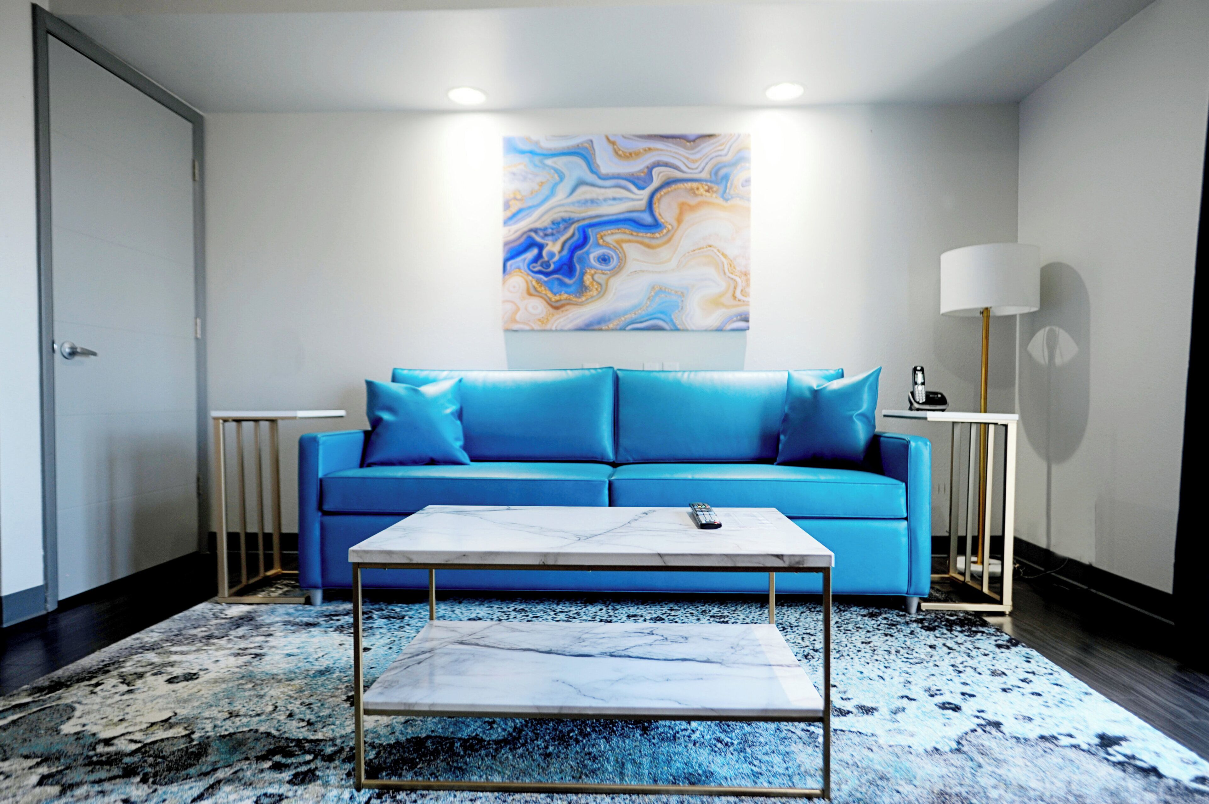 Una sala de estar moderna con un sofá azul, una mesa de centro de mármol y un cuadro abstracto grande en la pared.