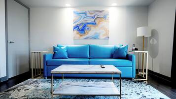 Una sala de estar moderna con un sofá azul, una mesa de centro de mármol y un cuadro abstracto grande en la pared.