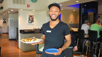 A person holding a plate of food and a stack of plates in a modern dining area with wooden flooring and contemporary furniture.