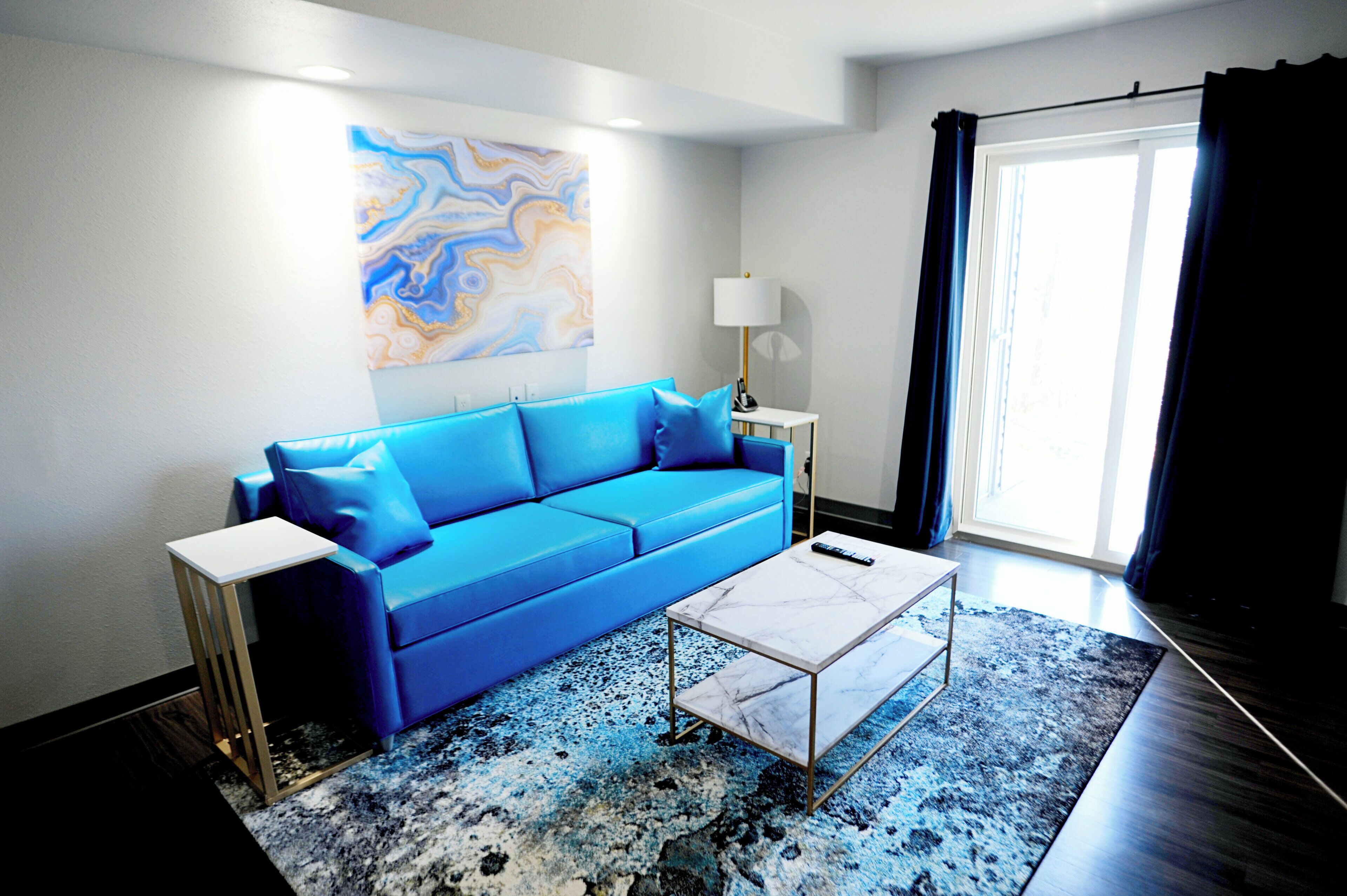 A modern living room with a blue sofa, a white coffee table, a floor lamp, and a large abstract painting on the wall.