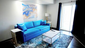 A modern living room with a blue sofa, a white coffee table, a floor lamp, and a large abstract painting on the wall.