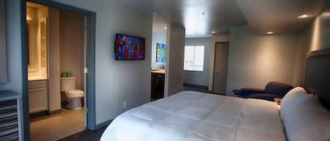 Una habitación de hotel moderna con una cama grande, televisor y baño con inodoro y lavabo.