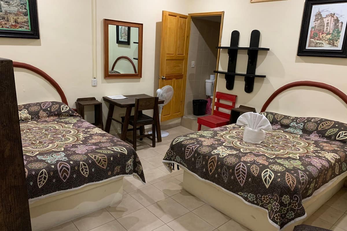 Habitación de hotel con dos camas, un escritorio, una silla, un espejo y una puerta.